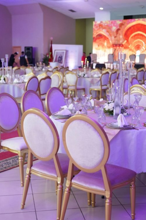 Luxurious banquet hall set for a grand event with elegant decor, purple lighting, and arranged tables.